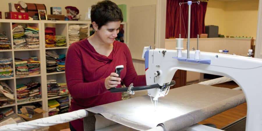 Smiling person works on a long arm sewing machine in her studio
